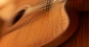 A close-up view of a hand pressing down on the strings of a wooden acoustic guitar.